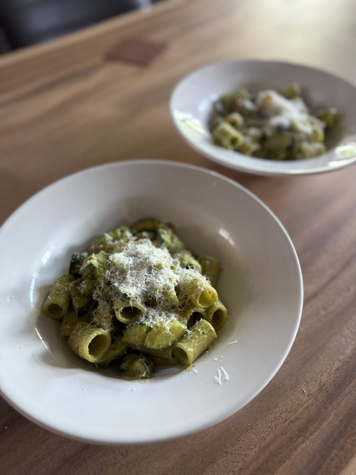 Close-up van een bord pasta pesto met gebakken courgette, grove rigatoni en een royale topping van Parmezaanse kaas.