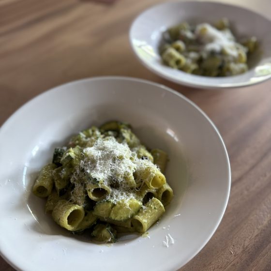 Close-up van een bord pasta pesto met gebakken courgette, grove rigatoni en een royale topping van Parmezaanse kaas.